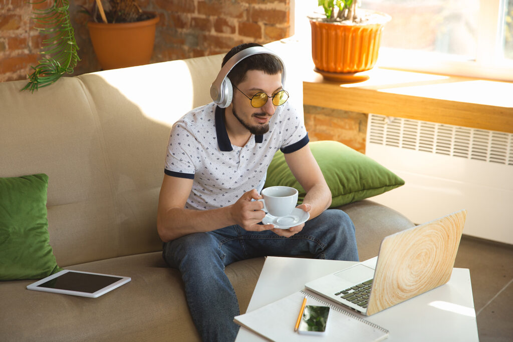 A person sitting in a cozy home office, taking a break to enjoy a cup of coffee and listen to music, surrounded by creative materials and work essentials.