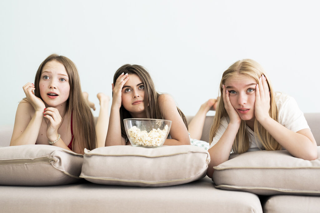 A group of friends watching a comedy show together, laughing heartily on a cozy couch with popcorn.