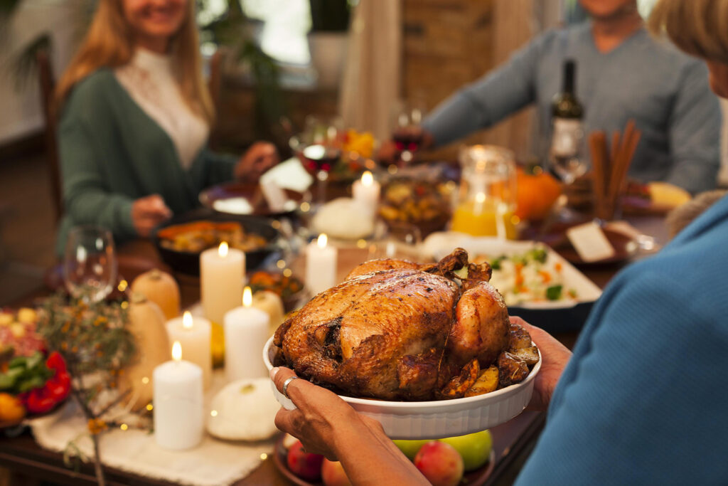 A festive table set with roasted turkey, mashed potatoes, and fall-themed decorations, surrounded by family members enjoying the feast.