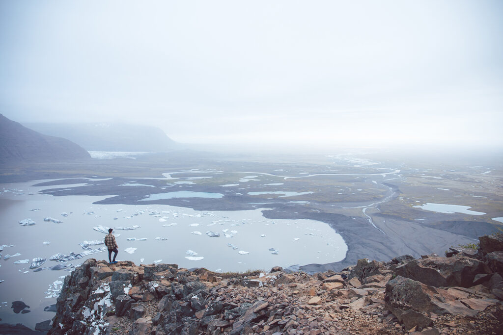 A dramatic landscape of jagged mountains, glacial lakes, and vast open plains in Patagonia, with a hiker standing in awe.