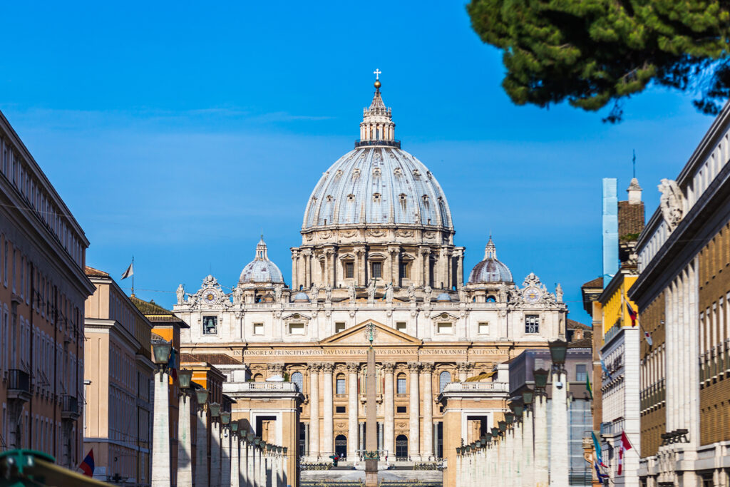 A panoramic view of St. Peter’s Basilica in Vatican City during sunrise, with soft golden hues illuminating its iconic dome and surrounding square.