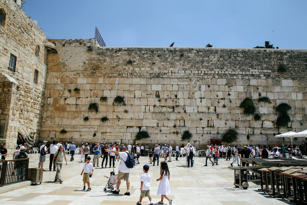 The Western Wall in Jerusalem, with people praying against the ancient stone, bathed in the warm glow of the setting sun.