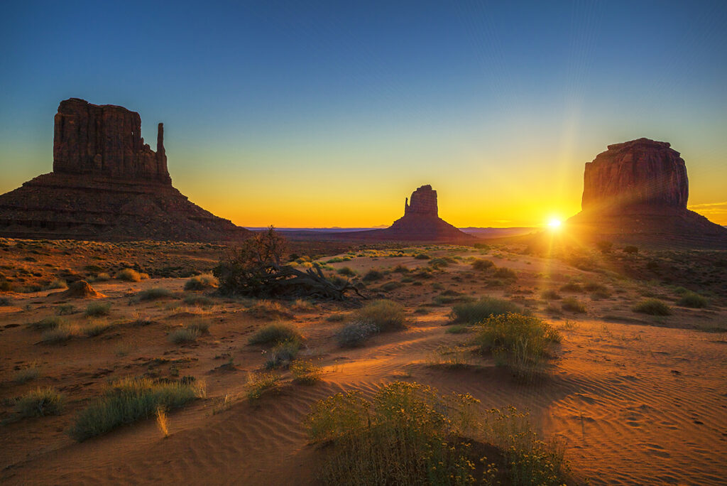 A vast desert landscape in Monument Valley, with towering red sandstone formations under a bright blue sky, showcasing the spirit of the American West.