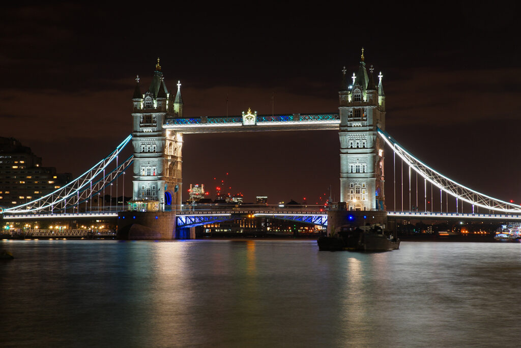 The iconic Tower Bridge in London, lit up at night against the dark sky, with the River Thames flowing underneath.