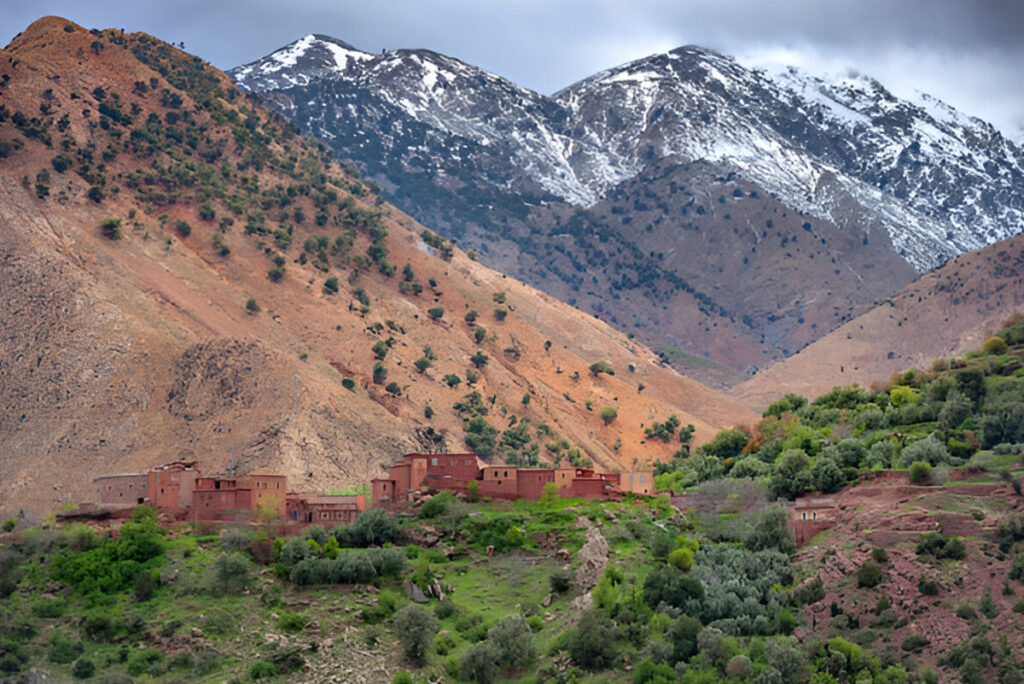 A stunning aerial view of the Atlas Mountains, with their snow-capped peaks overlooking a lush valley, with traditional Berber villages nestled in the foothills.